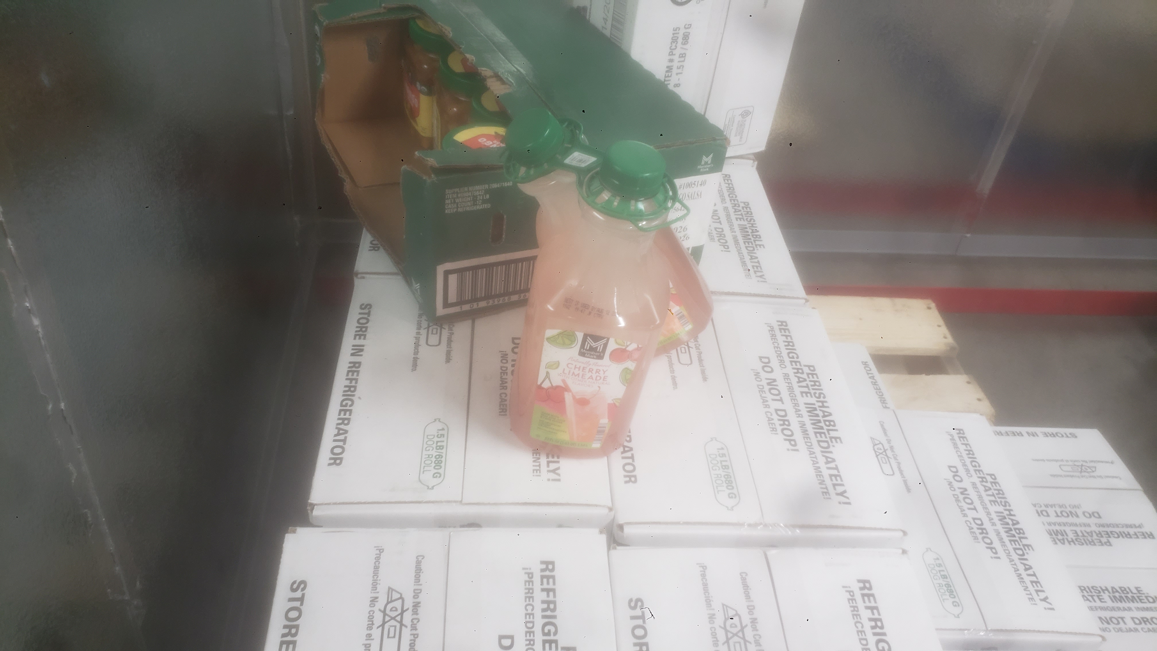 Bottles of cherry limeade and jars of mango salsa in a shipping tray on top of boxes of pet food.